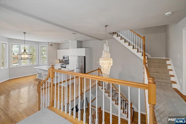 stairway with wood finished floors and a notable chandelier