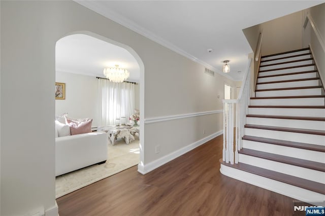 stairway featuring baseboards, visible vents, arched walkways, wood finished floors, and crown molding