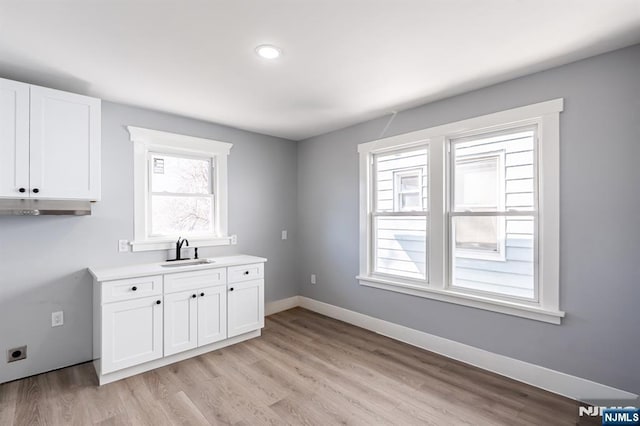 washroom with light wood-type flooring, a sink, and baseboards