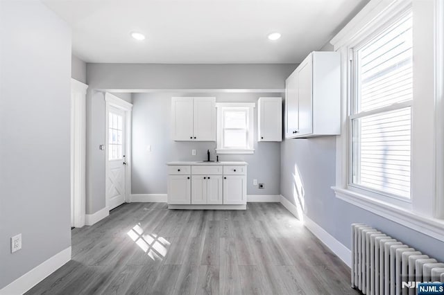 kitchen featuring recessed lighting, white cabinetry, light wood-style floors, baseboards, and radiator heating unit