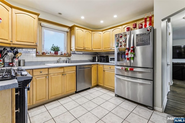 kitchen featuring light tile patterned floors, tasteful backsplash, light countertops, appliances with stainless steel finishes, and a sink