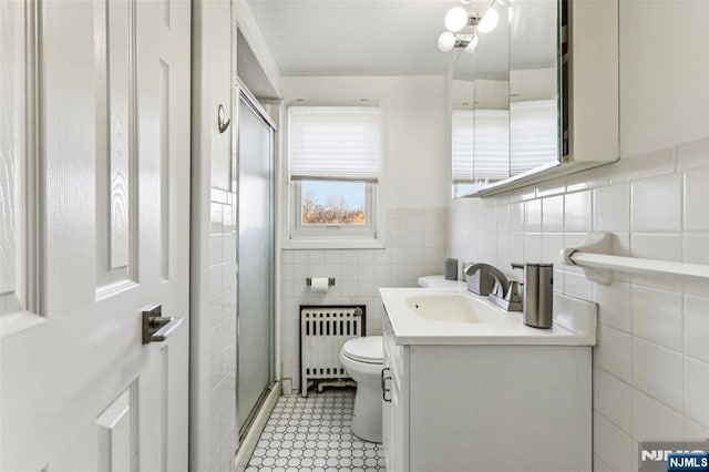 bathroom featuring a stall shower, toilet, radiator heating unit, vanity, and tile walls