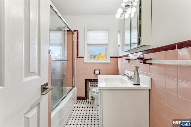 bathroom with tile patterned flooring, toilet, bath / shower combo with glass door, vanity, and tile walls