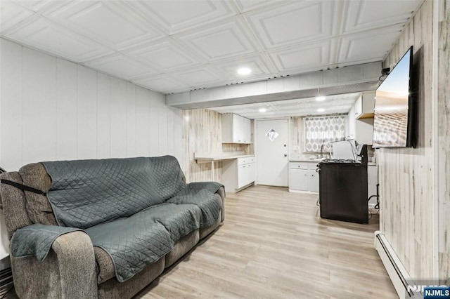 living room featuring an ornate ceiling, light wood-style floors, a baseboard radiator, and wood walls