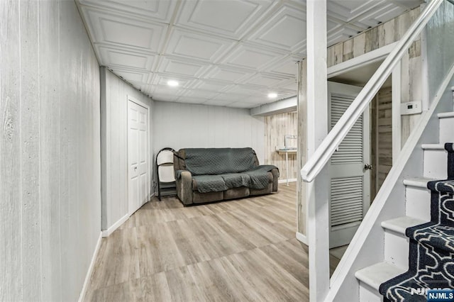 sitting room featuring light wood-style flooring, wood walls, baseboards, stairway, and an ornate ceiling