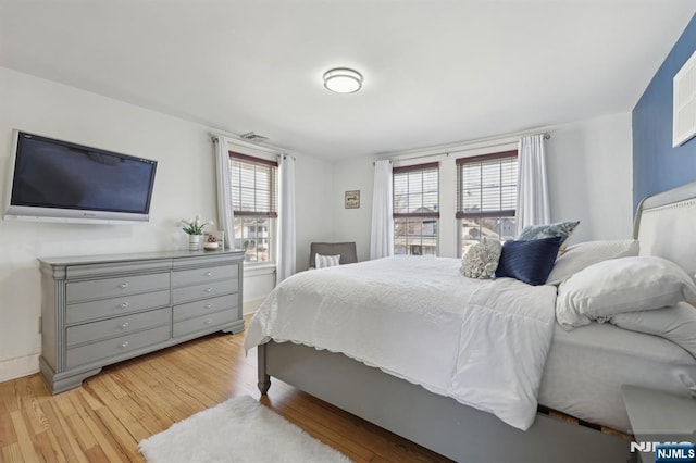 bedroom with multiple windows, light wood-type flooring, and baseboards