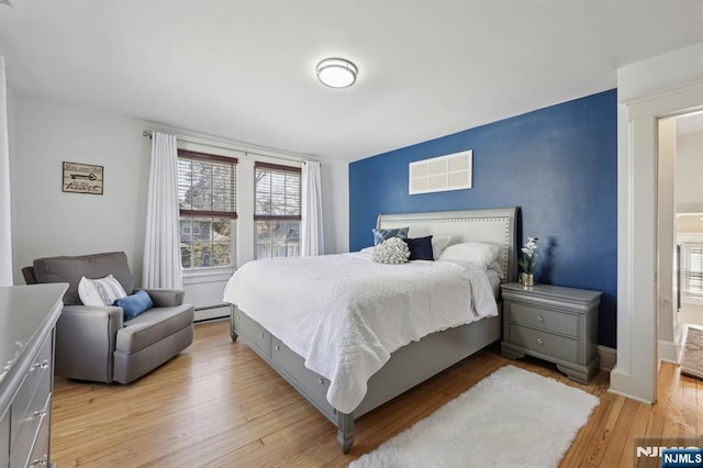 bedroom featuring light wood-style flooring, a baseboard heating unit, an accent wall, visible vents, and baseboards