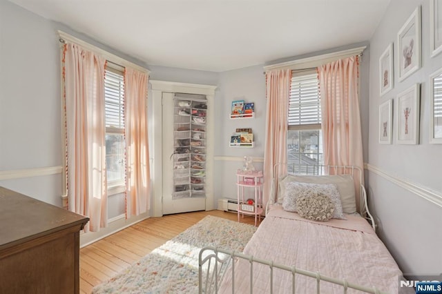 bedroom with light wood-style floors, multiple windows, and baseboard heating