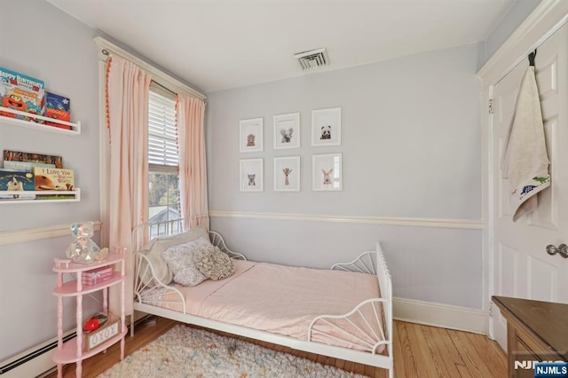 bedroom with baseboards, visible vents, a baseboard heating unit, and wood finished floors