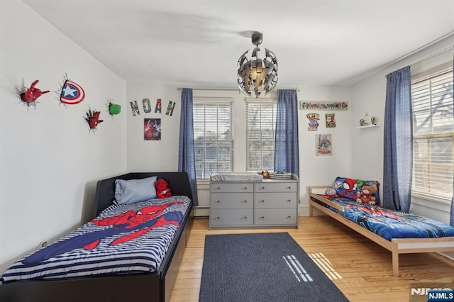 bedroom featuring baseboard heating, light wood finished floors, and an inviting chandelier