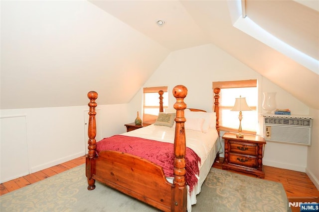 bedroom featuring lofted ceiling, a wall unit AC, wood finished floors, and baseboards