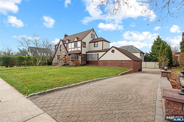 view of front facade featuring brick siding, fence, driveway, a front lawn, and a chimney