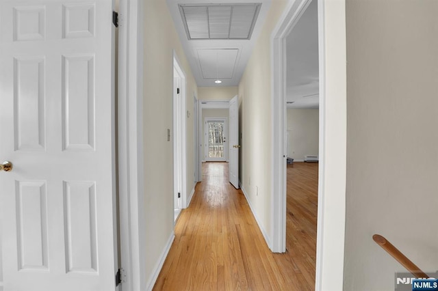 corridor featuring attic access, visible vents, baseboards, light wood-style floors, and a baseboard heating unit