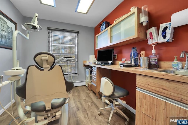 office space featuring light wood-type flooring, a baseboard radiator, baseboards, and a sink