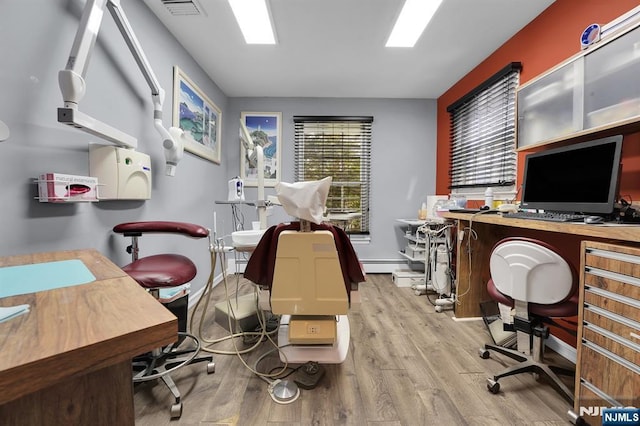 office area featuring a baseboard heating unit, a wealth of natural light, visible vents, and wood finished floors