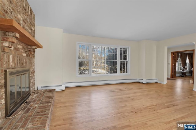 unfurnished living room with a baseboard heating unit, a fireplace, baseboards, and wood finished floors