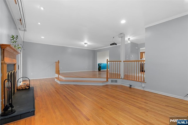 spare room featuring light wood-style floors, baseboards, a fireplace with raised hearth, and crown molding