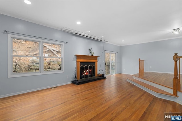 unfurnished living room with a warm lit fireplace, visible vents, baseboards, wood finished floors, and recessed lighting