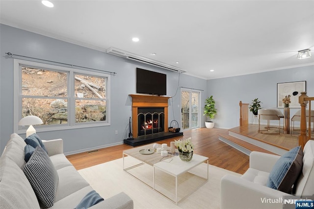 living area featuring a lit fireplace, recessed lighting, wood finished floors, and crown molding