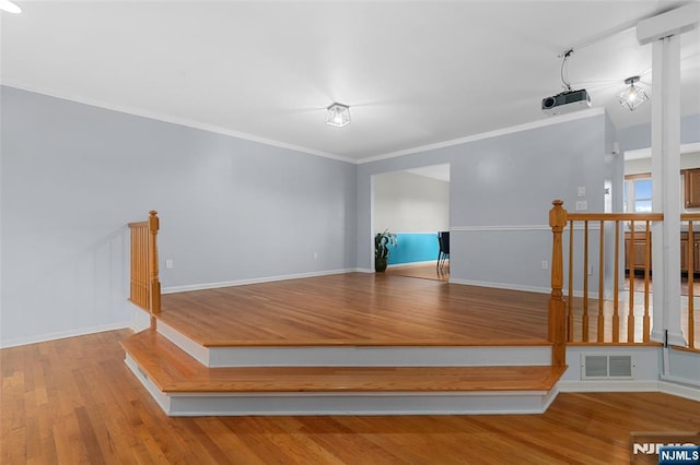 interior space with baseboards, visible vents, wood finished floors, and ornamental molding