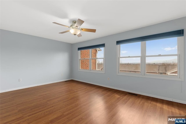 spare room featuring visible vents, ceiling fan, baseboards, and wood finished floors