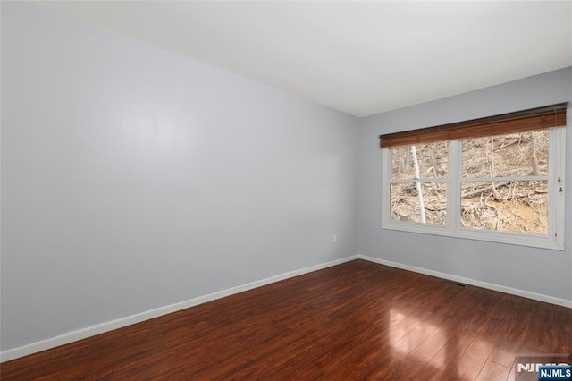 empty room featuring dark wood-style flooring, visible vents, and baseboards