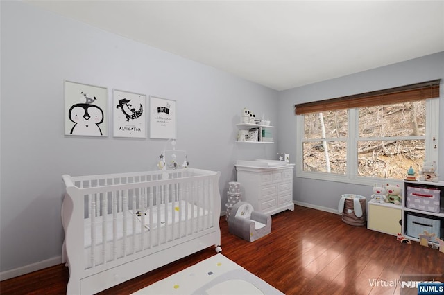 bedroom featuring a crib, baseboards, and wood finished floors