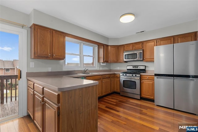 kitchen with stainless steel appliances, visible vents, a sink, a peninsula, and hardwood / wood-style flooring