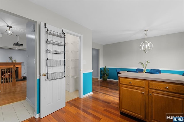 kitchen featuring light countertops, hanging light fixtures, brown cabinetry, wood finished floors, and baseboards