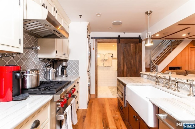 kitchen featuring a barn door, high end stove, under cabinet range hood, white cabinets, and light wood-type flooring