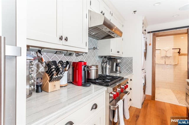 kitchen with white cabinets, stacked washer and dryer, stainless steel stove, and under cabinet range hood