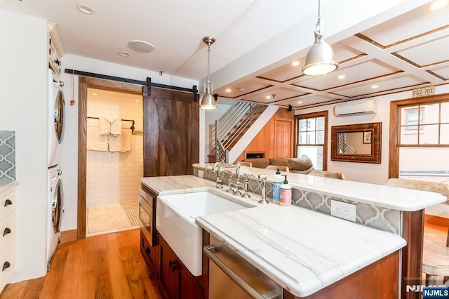 kitchen with stacked washer and dryer, light wood-style flooring, a barn door, coffered ceiling, and a wall mounted air conditioner