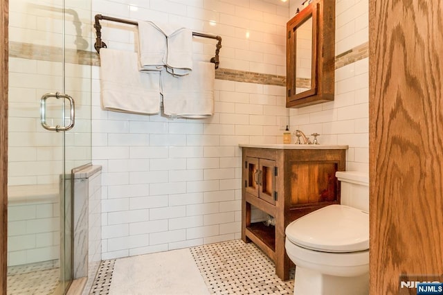 bathroom with tile patterned flooring, toilet, vanity, tile walls, and a shower stall