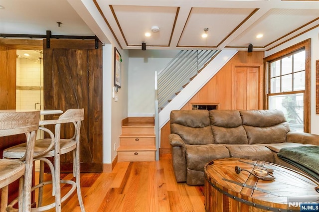 living area with light wood finished floors, a barn door, stairway, and coffered ceiling