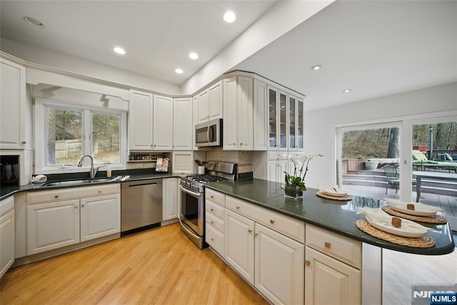 kitchen with stainless steel appliances, decorative backsplash, a sink, light wood-type flooring, and a peninsula