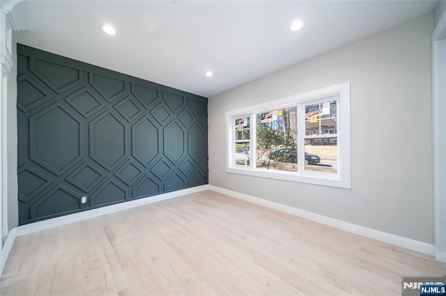 spare room featuring an accent wall, recessed lighting, light wood-type flooring, and baseboards