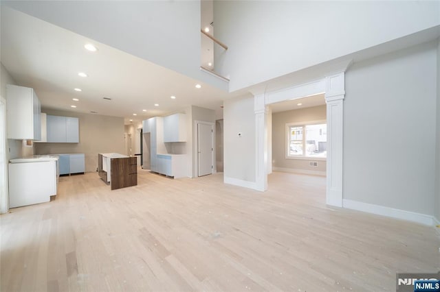 unfurnished living room with recessed lighting, a towering ceiling, baseboards, light wood finished floors, and ornate columns