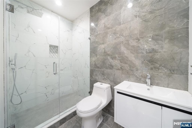 full bathroom featuring vanity, a marble finish shower, toilet, and tile walls