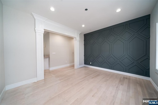 spare room with an accent wall, light wood-style floors, decorative columns, and baseboards