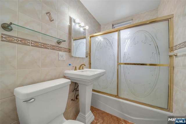 bathroom featuring toilet, combined bath / shower with glass door, and tile walls