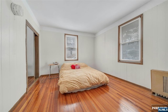 bedroom with multiple windows, light wood-type flooring, a closet, and radiator