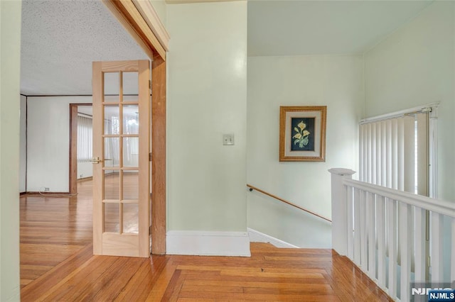 hall with a textured ceiling, wood finished floors, an upstairs landing, and baseboards