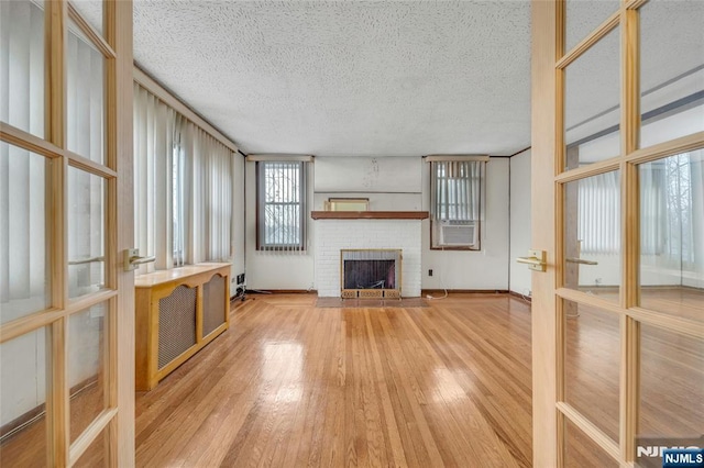 unfurnished living room featuring a textured ceiling, a fireplace, wood finished floors, and french doors