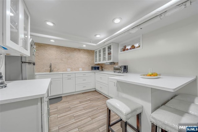 kitchen with a peninsula, a sink, light countertops, decorative backsplash, and a kitchen bar