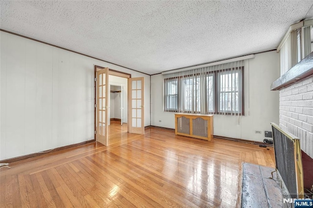 unfurnished living room featuring wood-type flooring, ornamental molding, a textured ceiling, french doors, and a fireplace