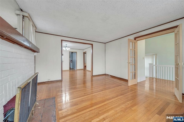 unfurnished living room featuring a textured ceiling, light wood-style flooring, a fireplace, baseboards, and ornamental molding