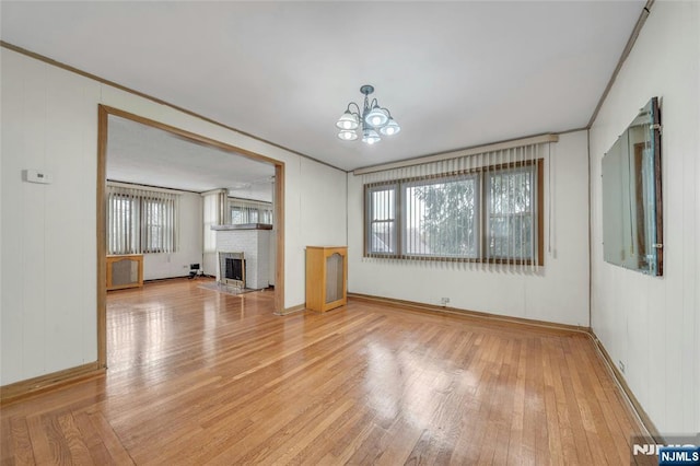 unfurnished living room with ornamental molding, light wood-type flooring, a notable chandelier, and a fireplace