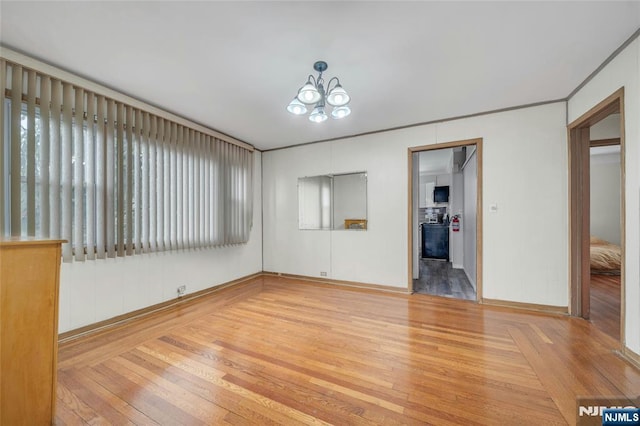 spare room featuring wood finished floors and an inviting chandelier