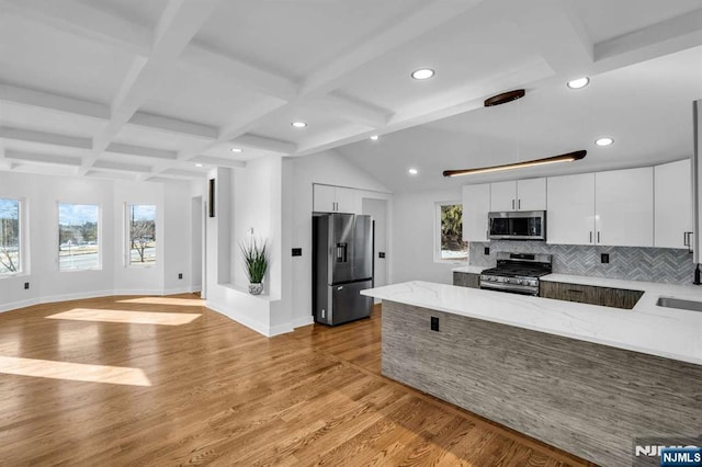 kitchen featuring stainless steel appliances, light wood-style floors, beamed ceiling, and a peninsula