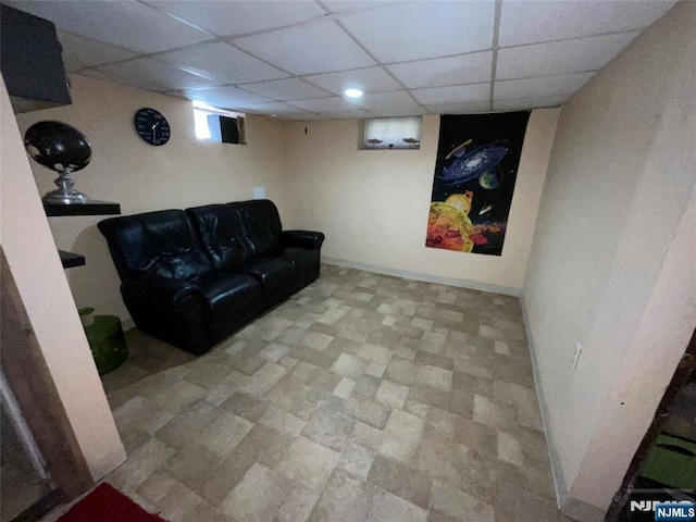 basement with a paneled ceiling and baseboards